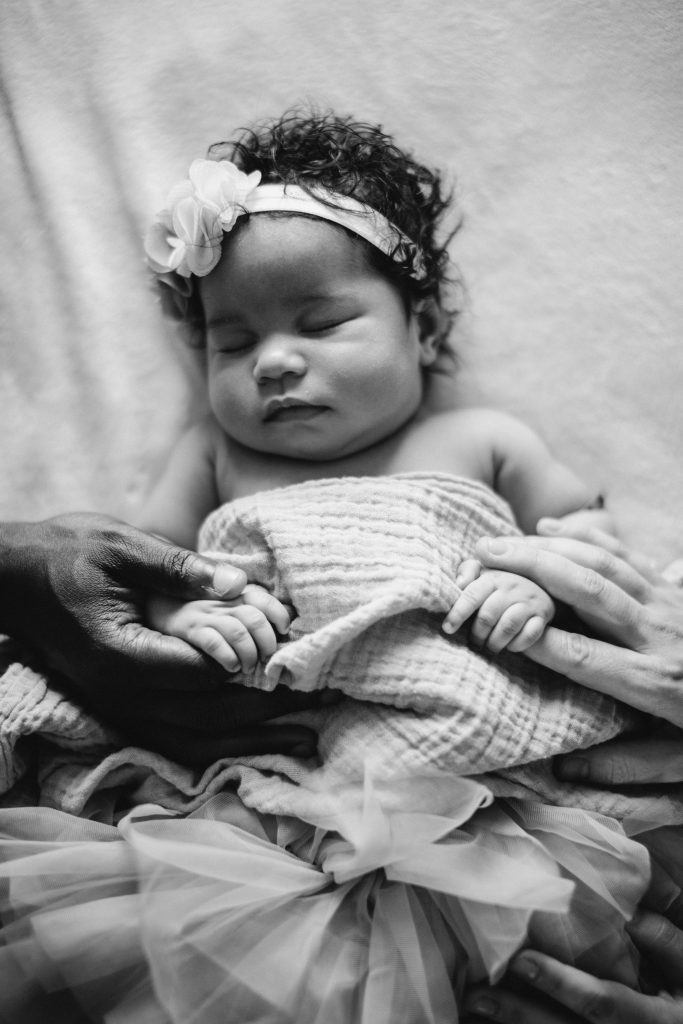 Newborn baby supported by caregivers’ hands, representing safety and connection in the first weeks at home